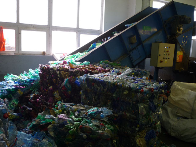 A to už je sousední firma PETKA CZ. Slisované lahve z balíků zde najíždí na pohyblivý pás a míří do drtiče. Předtím je nutné vytřídit lahve z PVC, které uživatelé často zaměňují, znečištěné lahve a speciální lahve např. na pivo, které jsou potaženy folíí nebo molekulárním filmem proti „unikání bublinek“. Na ty zatím uspokojivá technologie neexistuje.