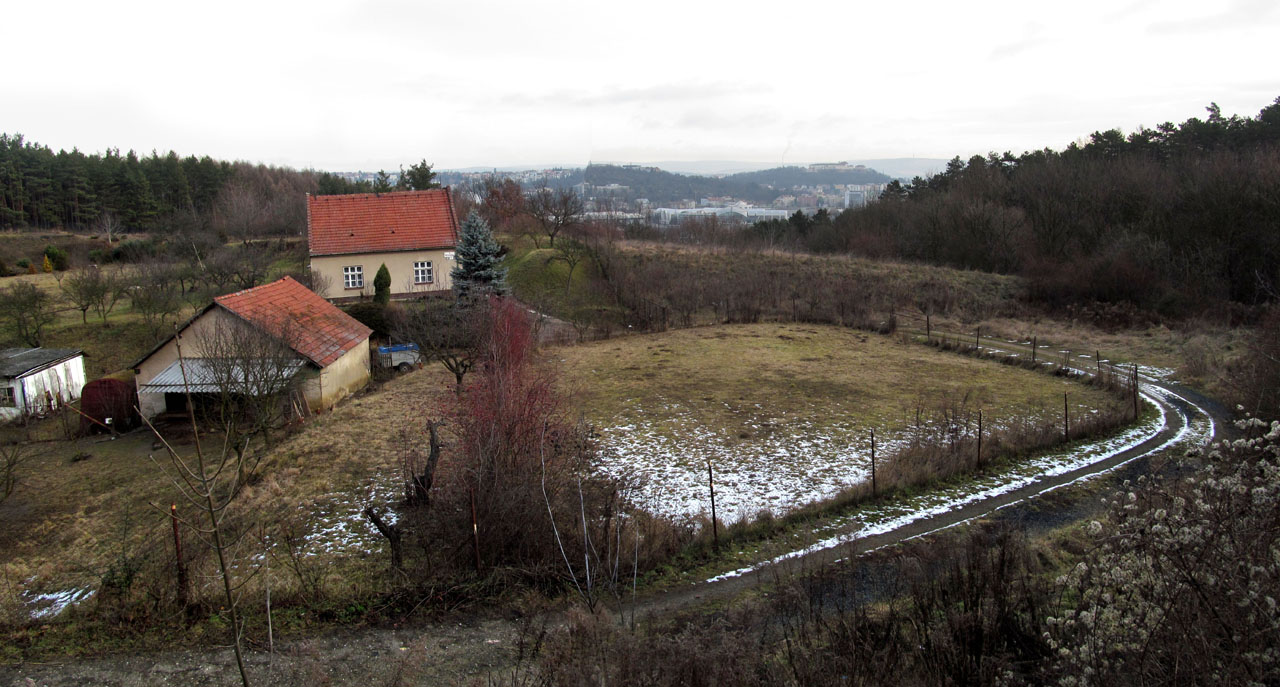Za hranou kopce čeká překvapení. Kdo by to byl řekl, že se tady, mezi moderními budovami a pustými roklemi, rozkládá útulný amfiteátr s venkovskou usedlostí. Idyla ovšem postupně mizí, obklíčena modernou.