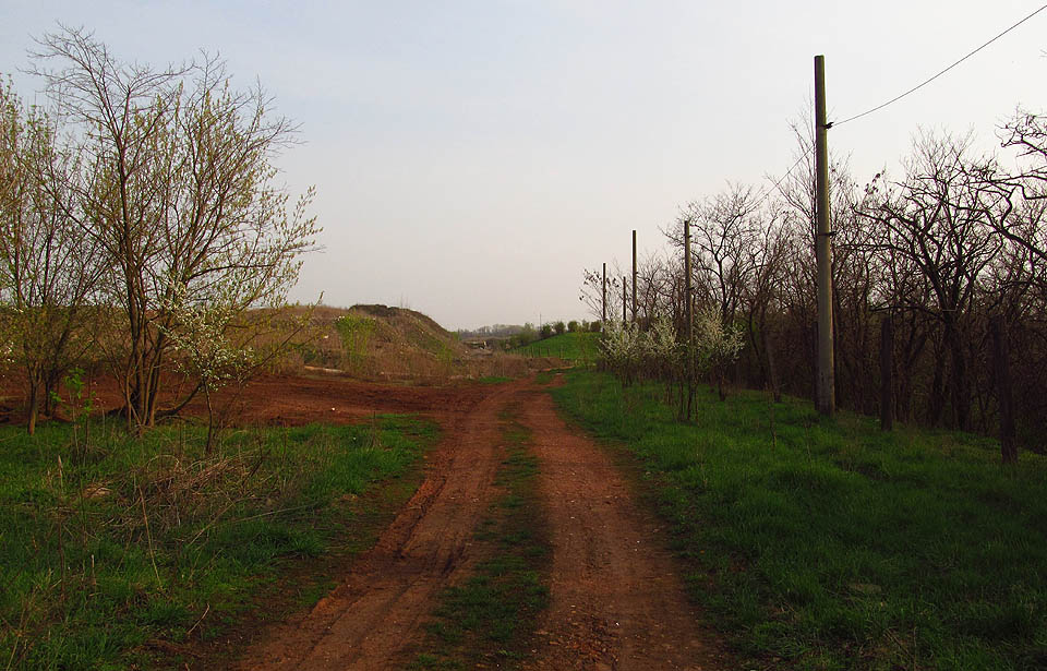Zadní cesta k černovické skládce vede okolo její rekultivované části. Červná barva země tu ostře kontrastuje se zelení okolních zahrádek.