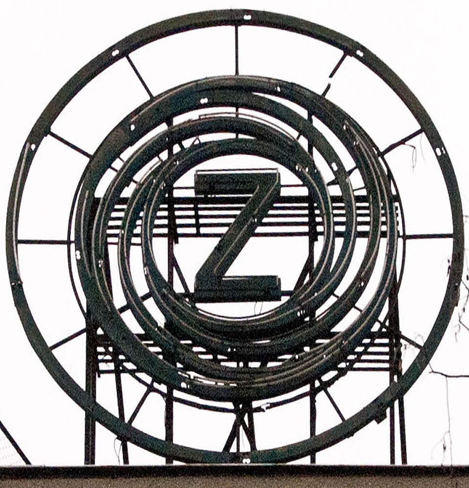 Logo Zbrojovky připomíná pohled do hlavně kulometu nebo pušky. V noci zářívaly modré neony nad mořem továrních světlíků a střech.