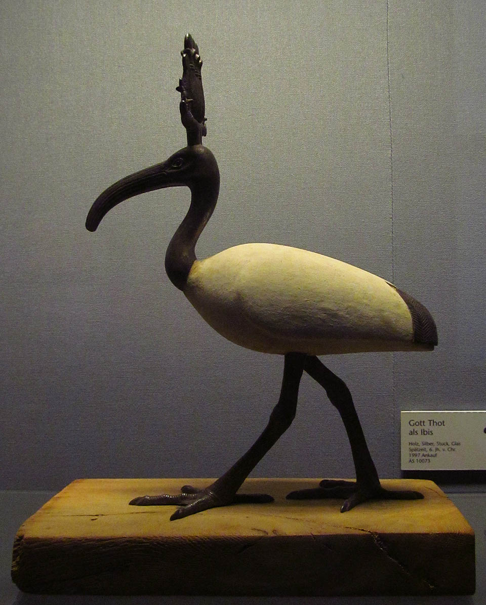 Bůh Thot v podobě ptáka ibise. Okolo stojí mumie lidské i zvířecí, sarkofágy a spousty dalších archeologických objevů.