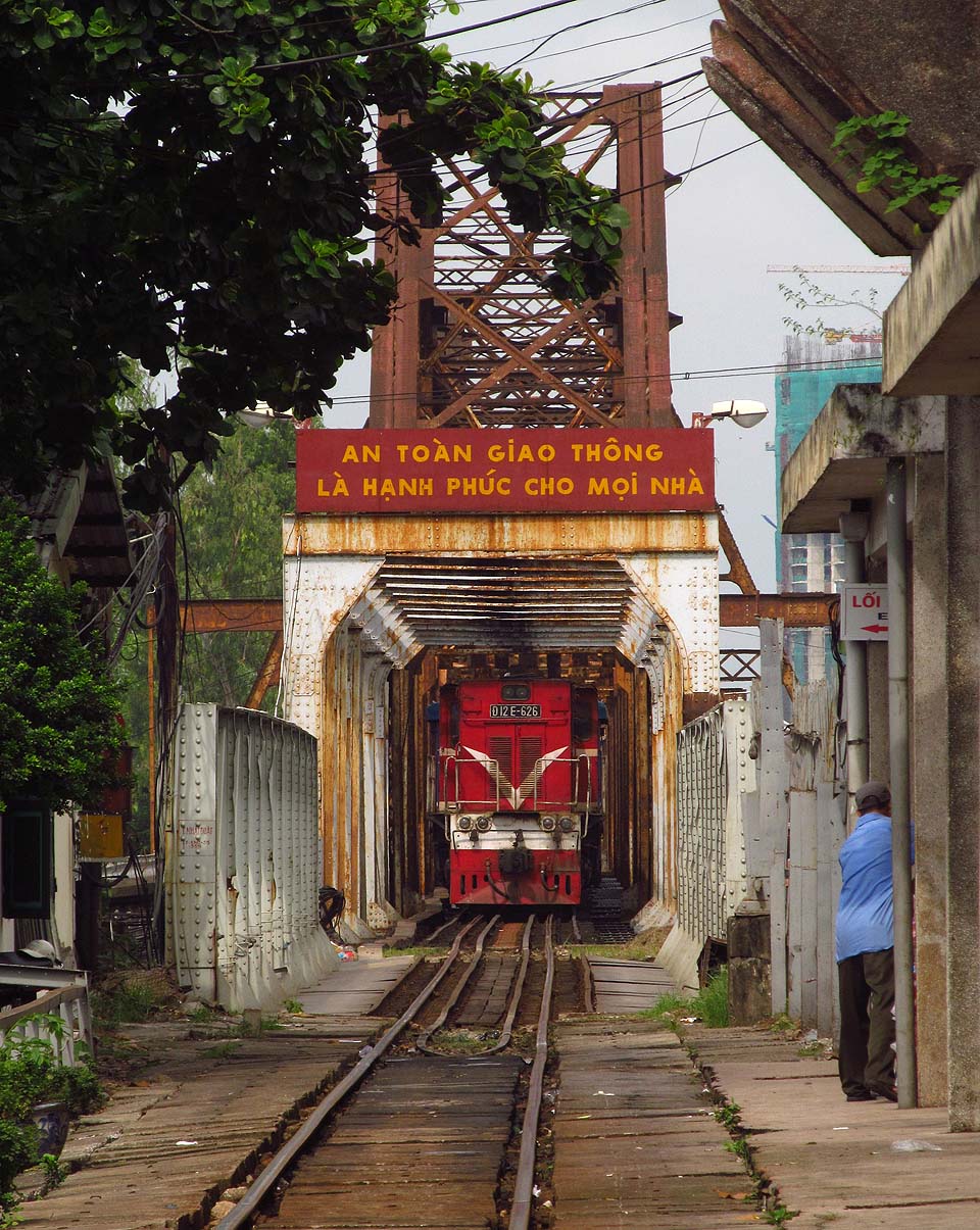 Lokomotiva D12E československé provenience na mostě přes Rudou řeku - jednom ze symbolů Vietnamu. Nápis podle překladače sděluje, že bezpečnost dopravy je štěstím pro každý domov.