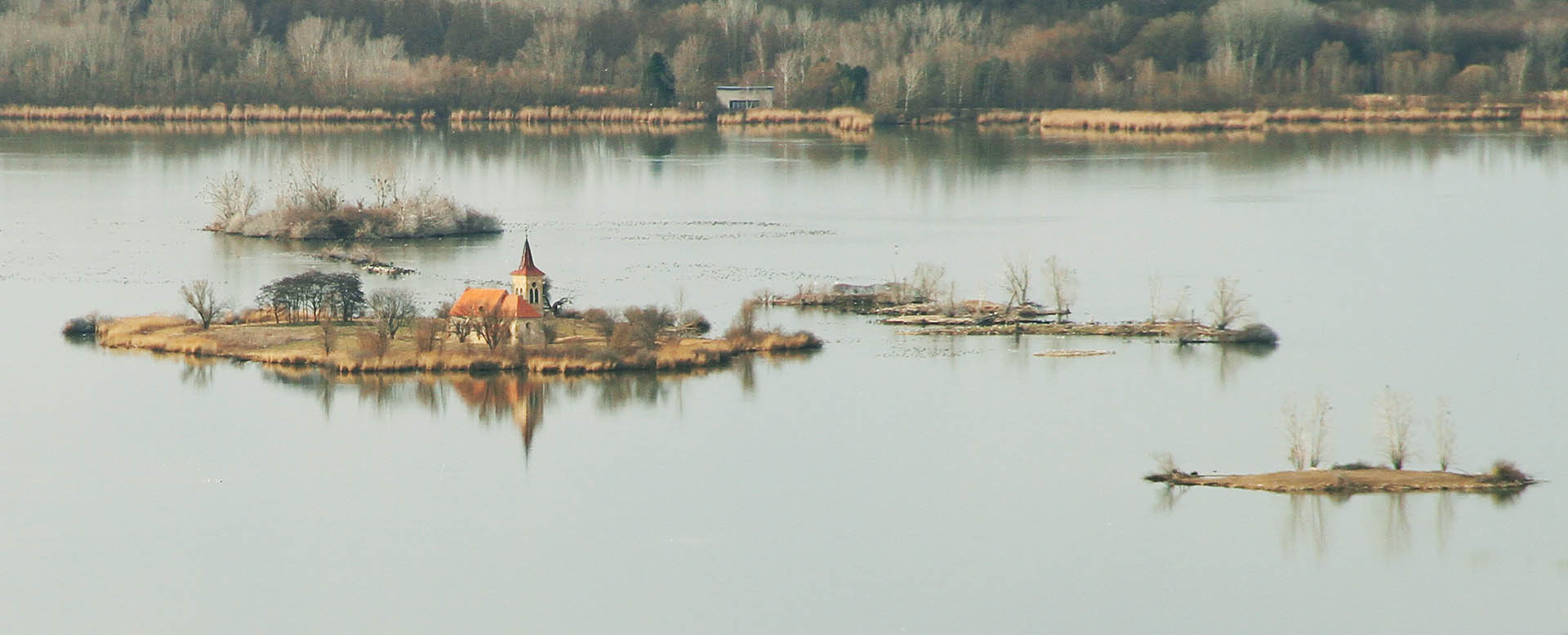 <a href=/Tema/Kostel%20sv.%20Linharta%20v%20Mu%C5%A1ov%C4%9B>Kostel svatého Linharta</a> nad zatopeným Mušovem chladně zářil nad hladinou jezera (pozorován z vyhlídky pod Trůnem).
