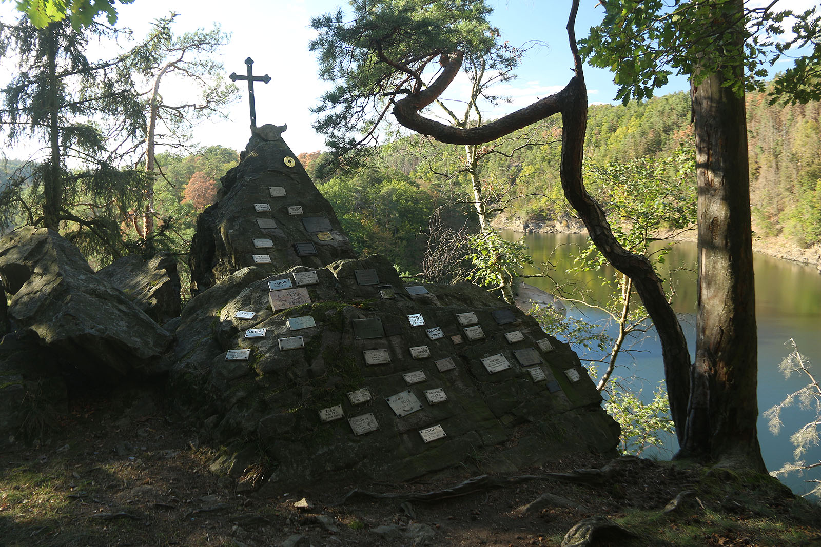 Trampský památník Maxův kříž na nás shlíží z protějšího břehu. Po létech jsme se k němu zase vydali - na lodi a pěšky strží.