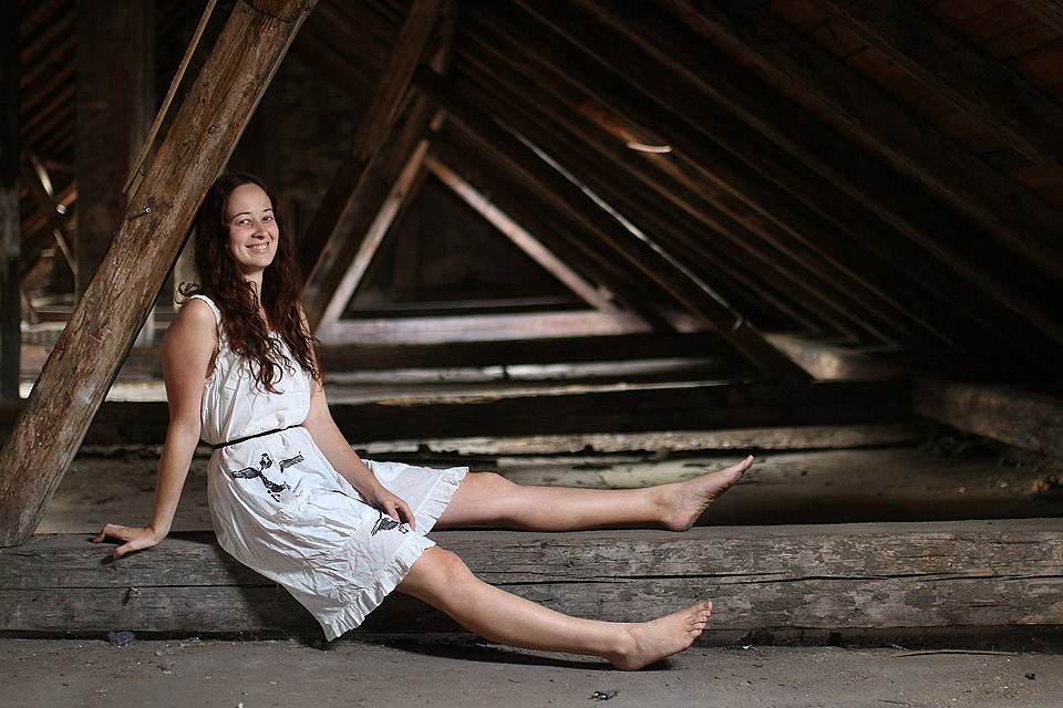 Bílé šaty s obrázky čápů a výraz á la Mona Lisa.