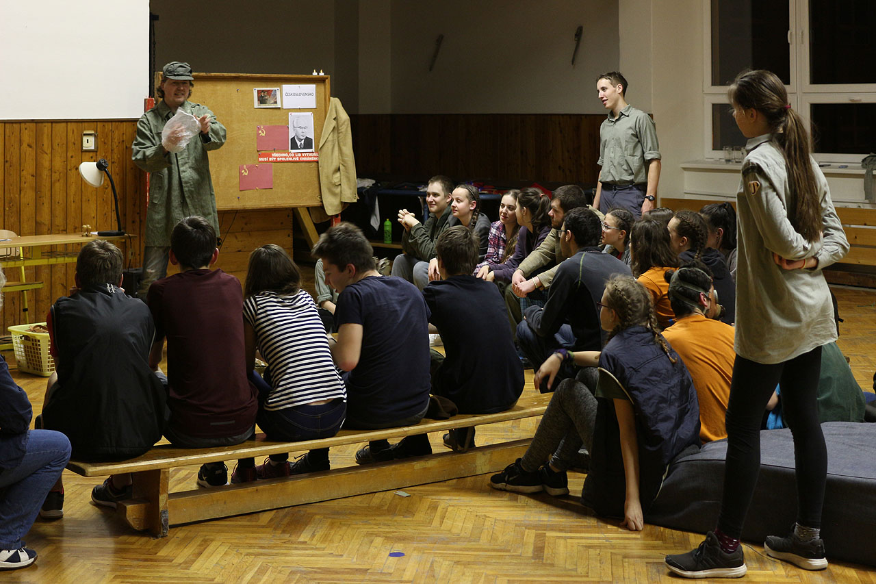 Strejda Vláček školí ve hře Cesta časem děti o materiálu budoucnosti - v éře Gustáva Husáka ukazuje třídě mikrotenový sáček.