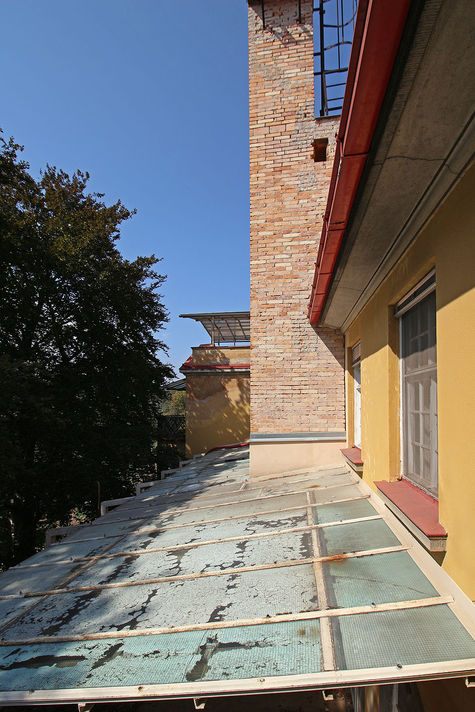 Drátosklová střecha terasy a necitlivě přistavěný komín dodávají vile na rozporuplné romantice.