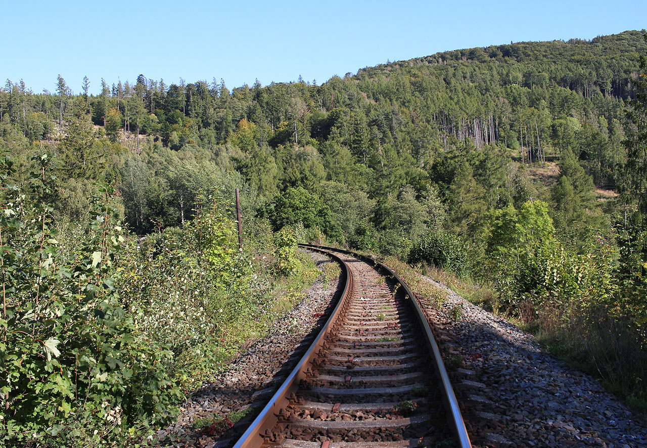 Železnice na vysokém náspu v údolí Milotického potoka prochází pod dohledem několika řad betonových řopíků.