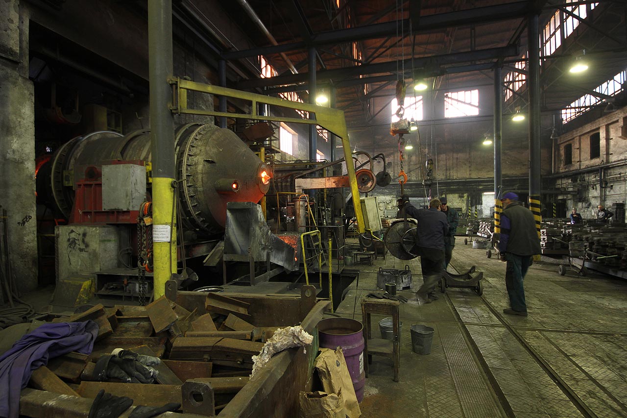 Přeprava zavěšené licí pánve od tavící pece na úzkokolejný vozíček.