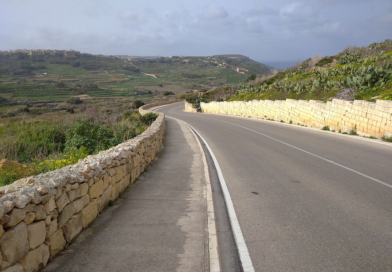 Klesáme dolů po ulici Triq Ir-Ramla. Protože Malta spíš než jako země působí jako jedno větší rozředěné město, jso tu chodníky i na silnicích ve volné krajině. 