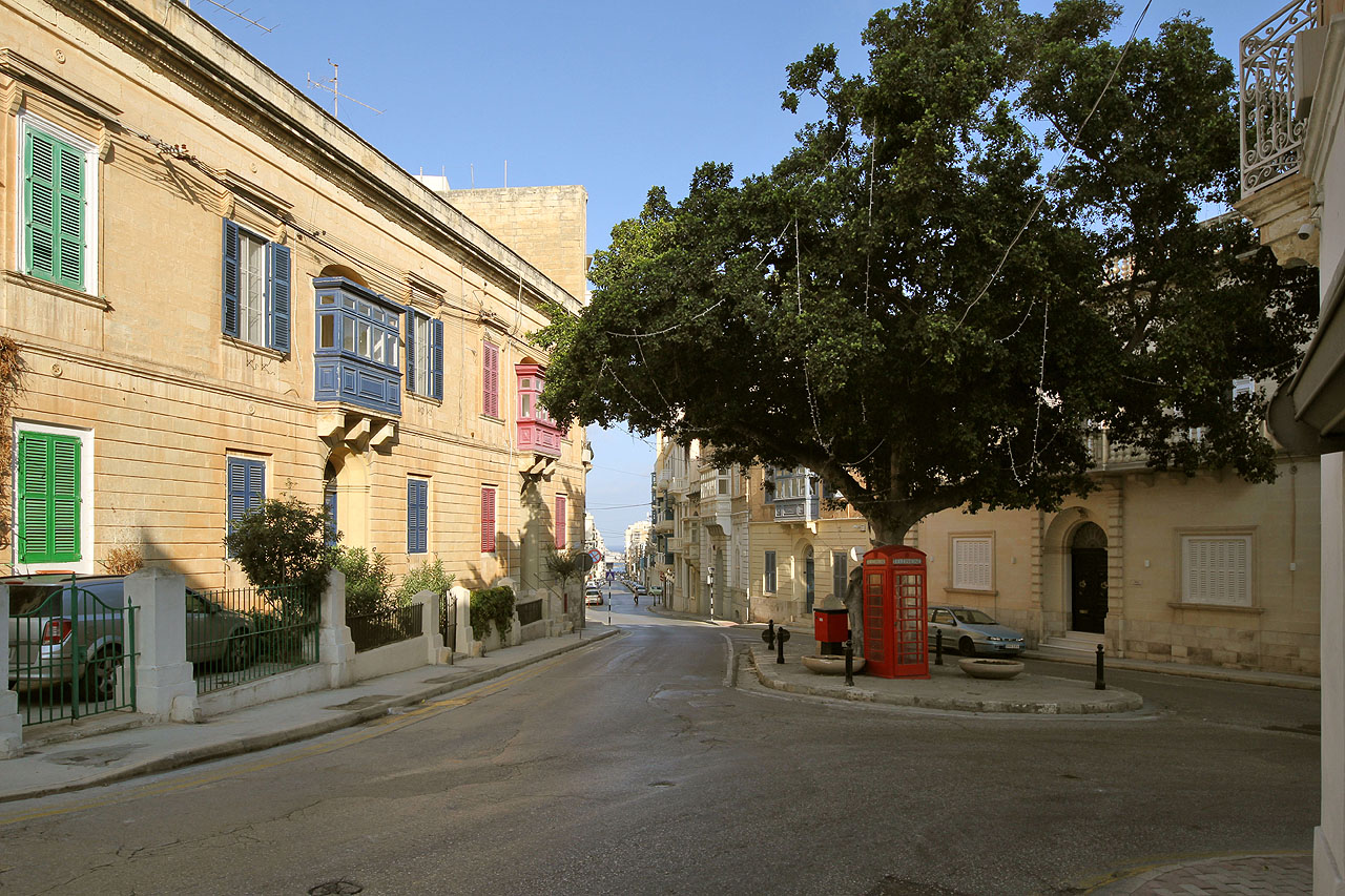 Bezejmenné nměstíčko na styku ulic Triq il-Kbira, Triq Santa Marija a Triq Sir Adrian Dingli s veřejným telefonem v britském stylu.