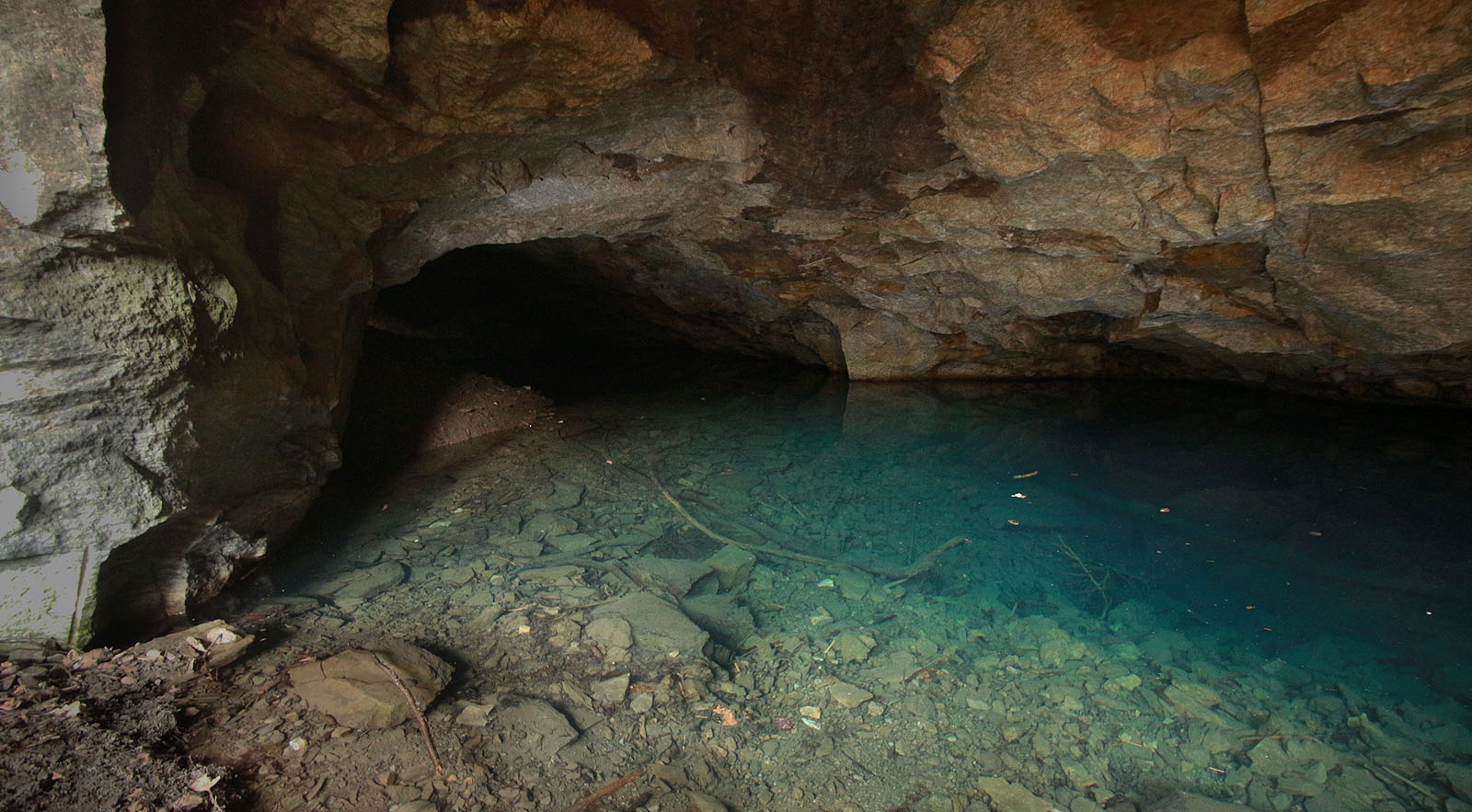 V létě může jít o vítané osvěžení, byť je barva vody jaksi nepřirozeně namodralá. Teď jsem se jen snažil nespadnout do vody při pořizování fotky ze dna zvláštní kaverny. Hromady materiálu před vstupem mě vedly k myšlence, zda se tu v minulosti netěžila třeba měděná ruda…
