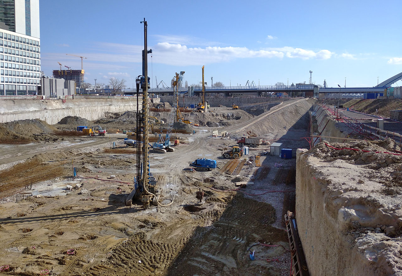 My ale míříme skrze zářivými reklamami vystalné nákupní doupě dál, do autentických zákoutí přístavů. Neprve je tnutné překonat zónu nikoho, kde už není přístav ale ještě není nákupní areál. Dno stavební jámy sahá zřejmě až pod hladinu Dunaje.