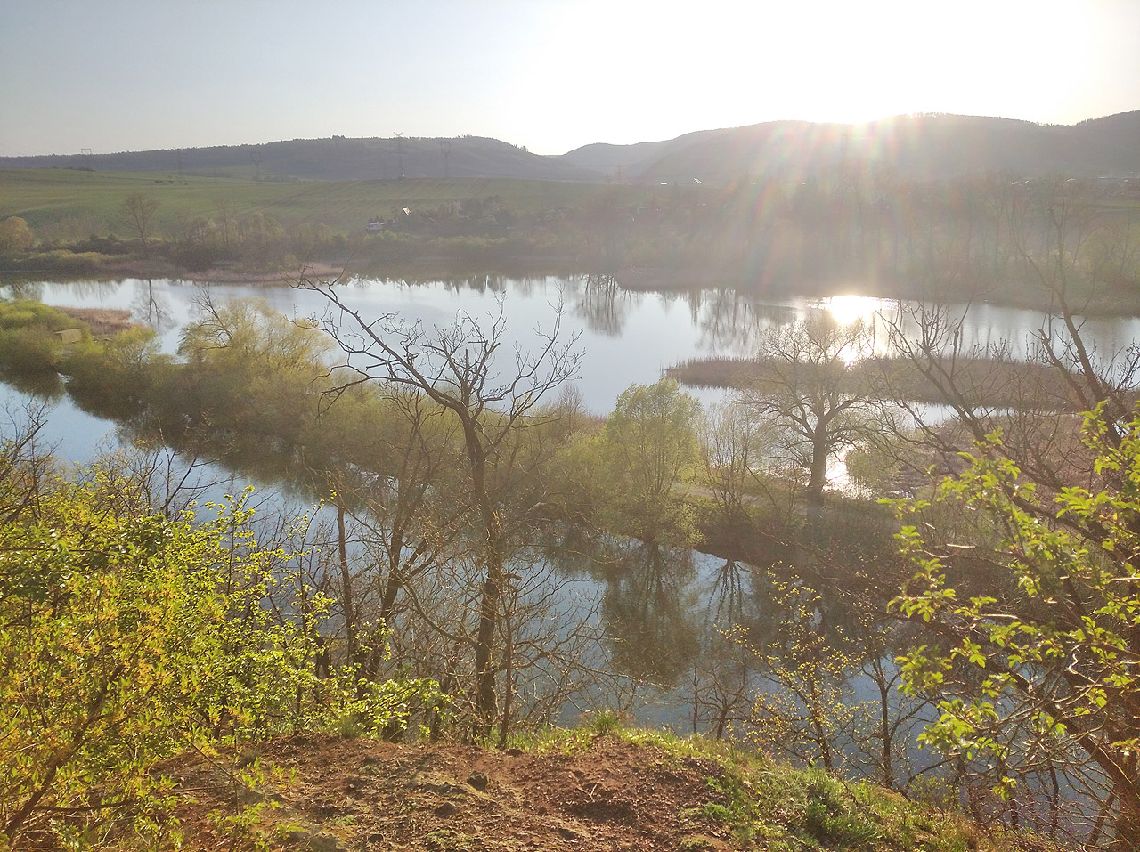 Pohled na rybník/bažinu na začátku vzdutí přehradního jezera při západu slunce. Vodní plocha je oddělená od zbytku přehrady, snad z důvodu chovu ryb. Nedaleko odsud se do vody také z nádrží čerpá kontinuálně síran železitý, který umožňuje vysrážení fosforu z eutrofizované vody, aby nemohl živit sinice ve vodě. Tryska s kalnou hmotou vstřikovanou do vody vypadá nechutně, díky ní je ale voda v přehradě už nekolik let krásně čistá.