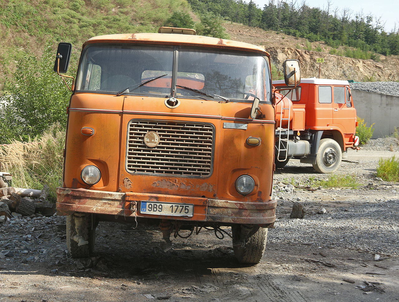 Zachovalé oranžové kropicí vozy značky LIAZ, jaké známe z dětství, zřejmě mají za úkol snižovat prašnost v době provozu lomu.