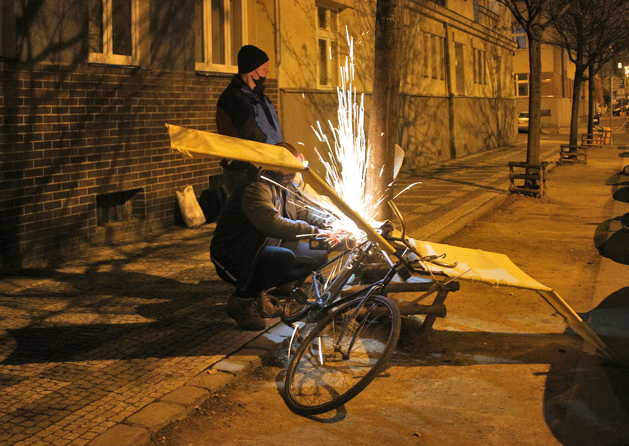 Post hoc. Zámečník odřezává od stromu Tleskačovo létající kolo, které tam vtipně zamknuli pražští Vontové. Prý nemá bez jejich svolení v uličkách, co dělat.