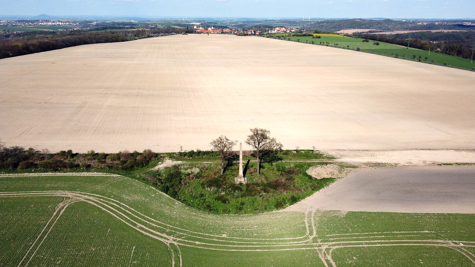Od obelisku šikmo doleva přes světlé pole ubíhaly koleje drážky vstříc smečenkému zámeckému parku. Dnes je někdejší existence železnice naprosto nevypozorovatelná.
