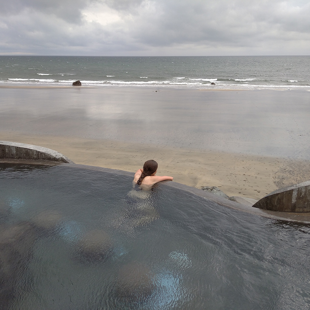Vyrazit jsme chtěli z Akureyri na severu, protože jsme oekávali příjemnější cestu směrem k jihu (jaká to chyba). Tam ale jezdí jen pár autobusů za den. Museli jsme si tak po cestě dát přestávku v městečku Akranes, kde jsme na pobřeží moře objevili docela naznámý horký prmaen Guðlaug. Jeho moderní přestavbu financovala městská rada z dědictví po bohatém rybáři, který odkázel peníze místní mládeži, aby mohla studovat rybářství. To ale jaksi vyšlo z módy, a tak se dnes mohou děti místo toho koupat střídavě ve vodě z horkého pramene a střídavě v chladném moři jako my.