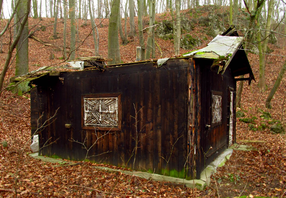 Opuštěná bouda nad osadou Koda možná patřila trampům nebo jeskyňářům. Zkratka FSC nade dveřmi sice svádí k úvahám nad dřevorubeckými certifikáty, její skutečný význam jsme ale nezjistili. Tam, kde byla podlaha, zeje temný otvor do hlubiny pohlcující postupně zbytek stavby.