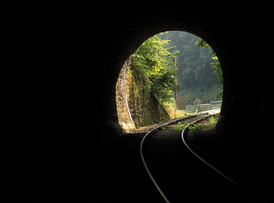 Pohled z chladivých útrob Bečovského tunelu na jeho severovýchodní portál a mosty přes silnici č. 20 (E49) a řeku Teplou. Tunel je po celé délce vyzděn kamennými bloky, které zajistily jeho trvanlivost již po 117 let.