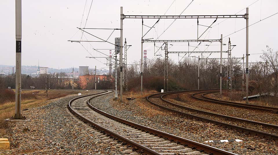 Na pohledu od západu je vidět vlastní odbočení jednokolejné Komárovské spojky (vlevo) od Vlárské dráhy vedoucí do <a href=/Tema/Brno-%C5%BDidenice%20%28%C5%BEst%29>Židenic</a>. Budova odbočky se skrývá v křoví za levým okrajem fotky, vzdálena 300 m a bez přímého výhledu.