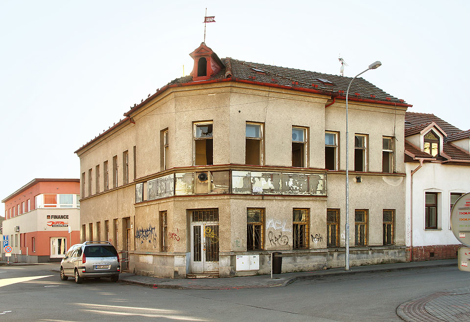 Nárožní dům s korouhví, vývěsním štítem zaniklého obchodu a vytlučenými okny patří k nejzajímavějším a současně nejodpudivějším objektům v ulici.
