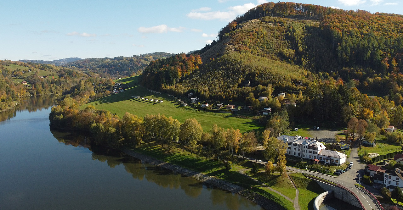 Pohled na hladinu vodní nádrže Bystřička znad její hráze s hotelem i vrcholem Klenovem v pravé části snímku.