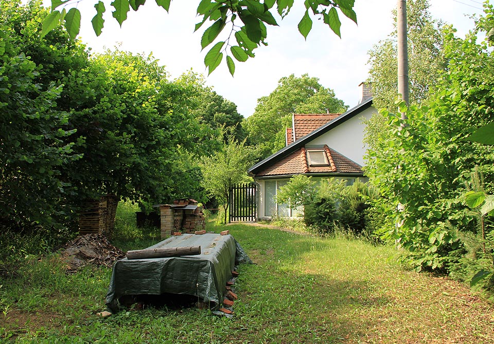 Pohled na bývalou zastávku Jehnice od jihu ze zárubu zrušené železniční trati. Z původní budovy je vidět jen zadní štít, ostatní části tvoří modernější přístavby.