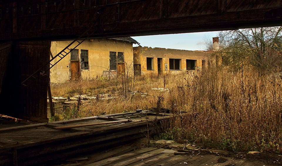 Na podlaze haly se válejí zřícené nosníky dřevěné střešní konstrukce. Pod sněhem, na dešti, větru a slunečním svitu se pomalu proměňují v prach.