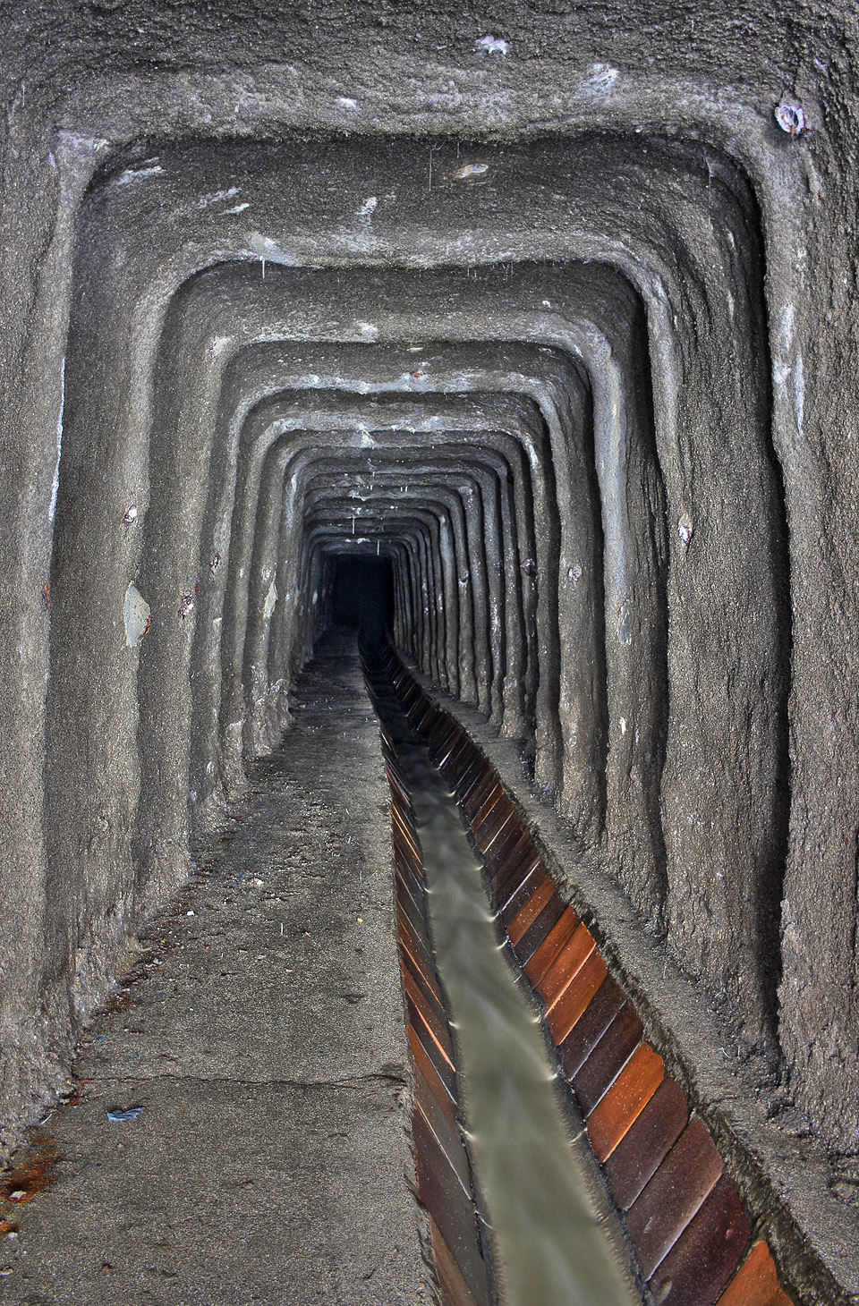 Vykročmě nyní vzhůru samotnou štolou. Betonový nástřik jen špatně ukrývá výztuž tvořenou zřejmě lichoběžníkovými hajcmany. Podlaha je za normálních podmínek suchá, ale často bývá pokrytá hmotou, kterou se raději ani neopovažujeme pojmenovat. Ze stropu visí krápníky, jak se vápenné složky betonu pomalu rozpouští v průsakové vodě.