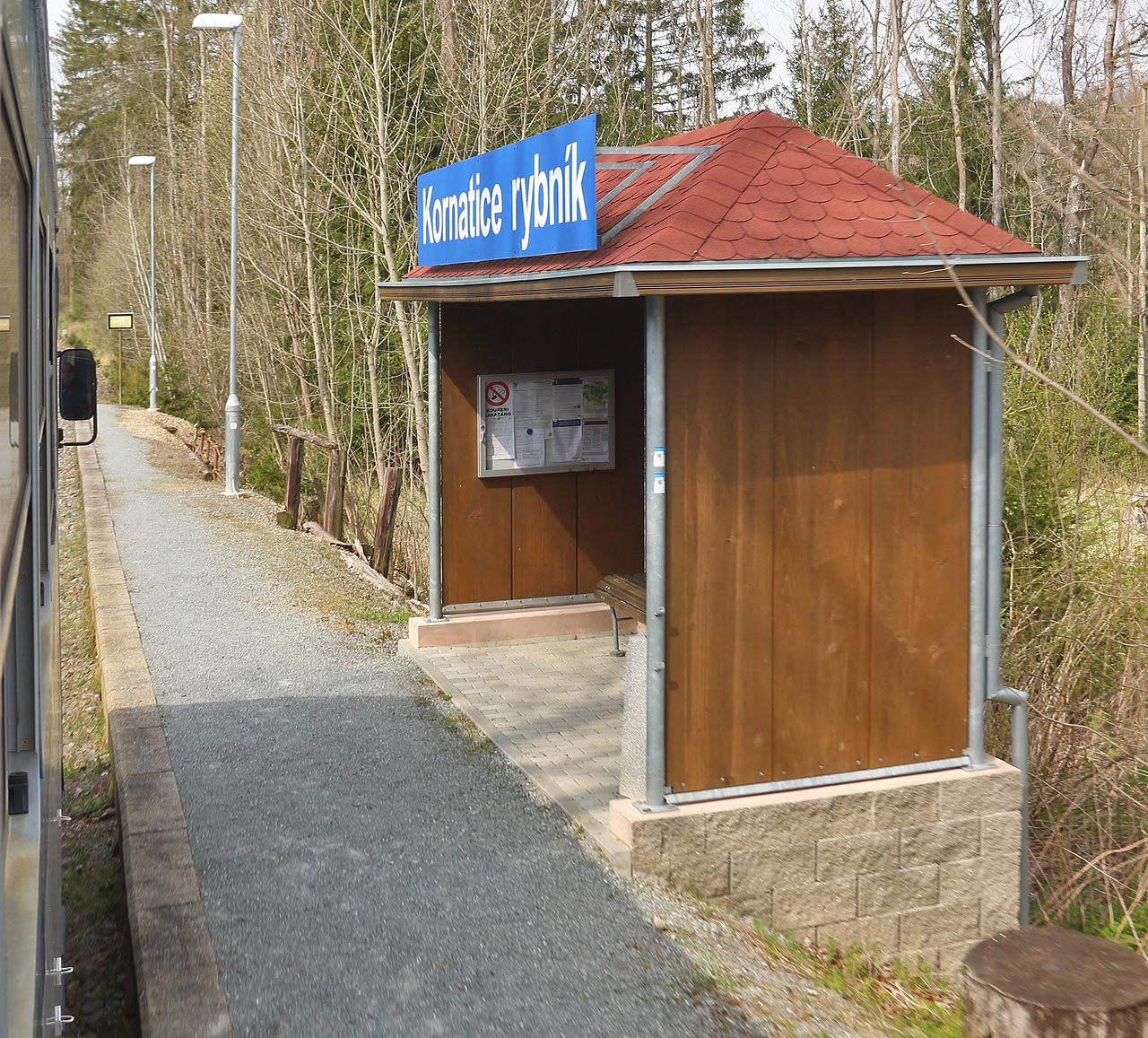 Pohled na dřevěný přístřešek zastávky Milínov z projíždějícího vlaku Os27824 v nedělním dopoledni 1. května 2022.