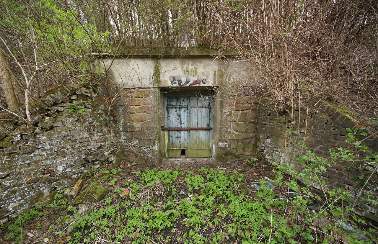 Dvojice opěrných zdí otevírá přístup ke kamennému portálu s dobře zabezpečenými masivními vraty.