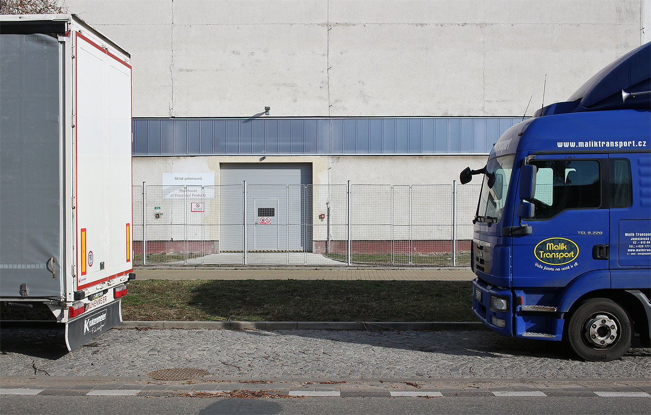 Vjezdové dveře do haly firmy Molitan. Zhruba tímto prostorem procházela šikmo úzkokolejka a vcházela do pozdějšího areálu Gumotexu. Provozů různých společností se tu nacházelo už na počátku 20. století několik a průmyslový areál postupně houstnul, drážka tak procházela úzkým koridorem mezi ploty a rozvětvovala se až na samotné pile.