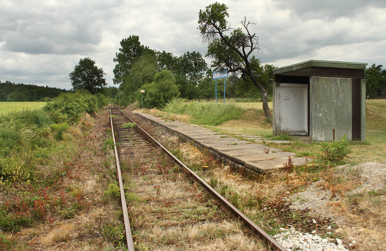 Pohled na železniční zastávku s moderní betonovou čekárnou od přejezdu směrem k severovýchodu.