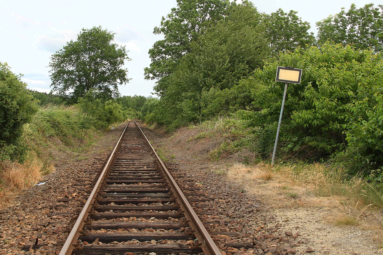 Cedulka označující konec nástupiště dlí daleko za koncem nástupiště v suché trávě a křoví. Cedulka označující konec nástupiště dlí daleko za koncem nástupiště v suché trávě a křoví.