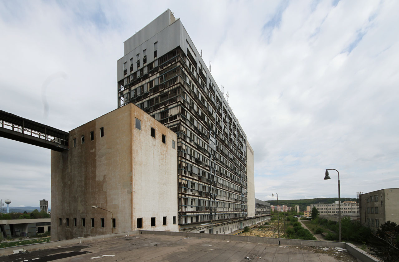 Pohled ze střechy nad krytou rampou pro vykládku obilovin a nakládku mouky nad trojicí kolejí železniční vlečky. Povšimněte si můstku spojujícího mlýn a silo na úrovni šestého patra. Pohled ze střechy nad krytou rampou pro vykládku obilovin a nakládku mouky nad trojicí kolejí železniční vlečky. Povšimněte si můstku spojujícího mlýn a silo na úrovni šestého patra.