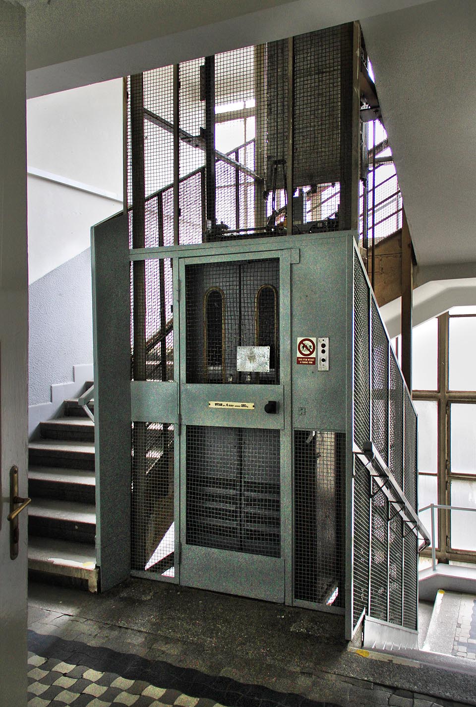 Do nižších pater můžeme sjet třeba výtahem. I když není původní, je se svými klecovými dveřmi s okénky krásně starobylý.