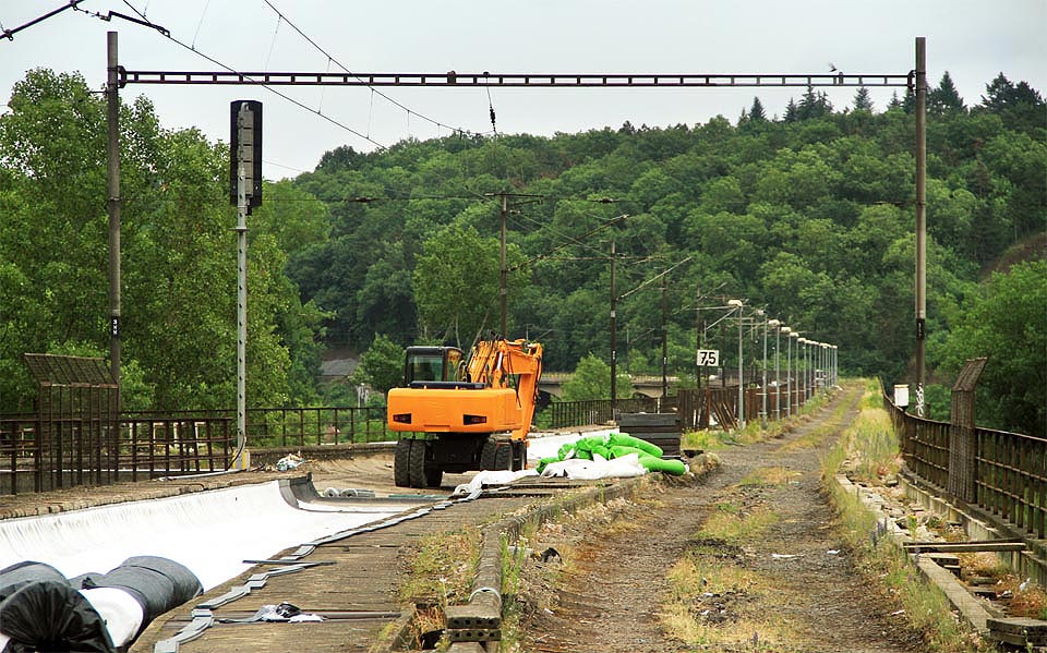 Bagr hlídá místo, kde se z Mostu intelignce měla oddělit jednokolejná spojka povádějící vlaky tunelem do Prokopského údolí, resp. později až do Berouna. Starší varianta je na plánku označená jako Hlubočepská spojka, novější pak jako spojka Žvahovská. Nejnovější tunel jako Tunel do Berouna.