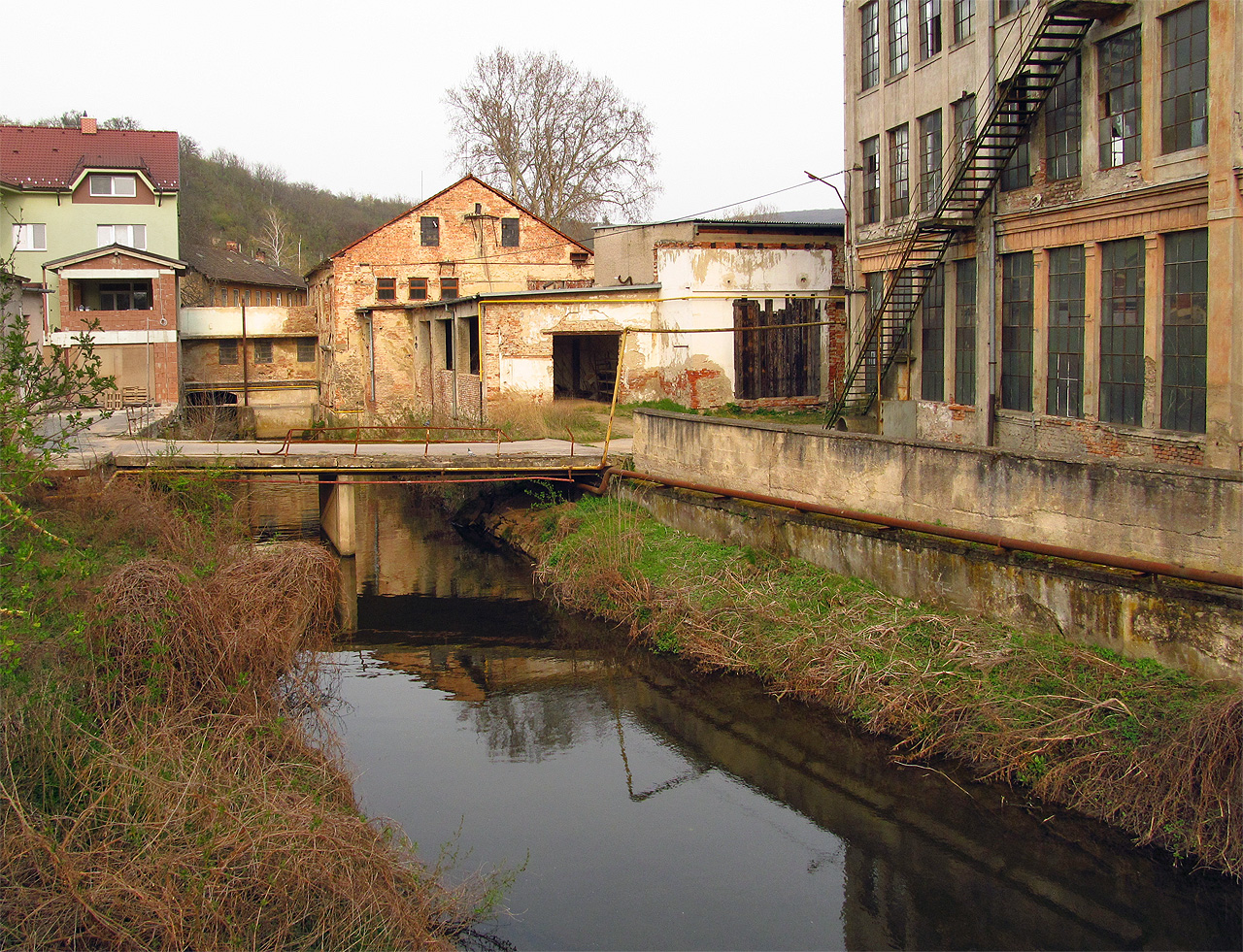 Pohled na Obřanský náhon z Obřanského mostu v roce 2014. Náhon prochází areálem <a href="/Tema/Esslerova přádelna Obřany">Esslerovy přádelny</a>, který pomalu ukusuje moderní civilizace. Sám most je zajímavý tím, že při jeho stavbě ve 30. létech 20. století se počítalo s protažením tramvajové trati až do Obřan a most byl proto silně naddimenzován. Ke zúžení nápadně široké vozovky na mostě došlo až při rekonstrukci v roce 2020.