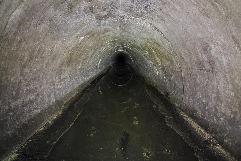 Šachty na povrch ustávají, místo betonových rour kráčíme nyní monolitickým tunelem. nad námi jsou desítky metrů zeminy, marně si lámeme hlavu, kam vlastně štola do hlubin země míří. Až později zjišťujeme, že jsme se stočili pod <a href=/Tema/Str%C3%A1nsk%C3%A1%20sk%C3%A1la>Stránskou skálu</a>.