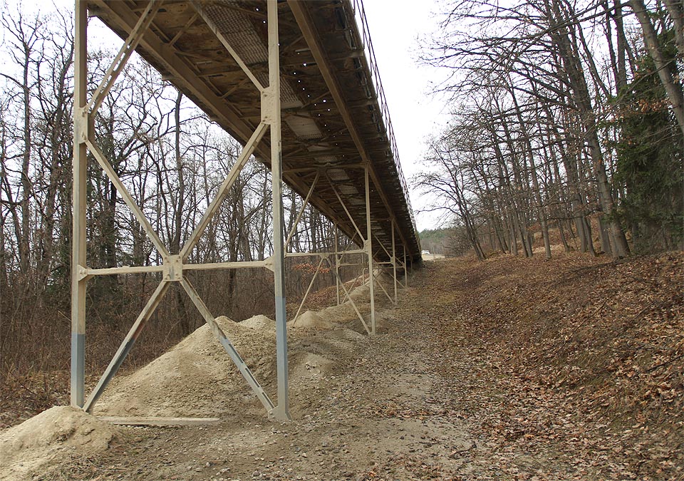 V posledním úseku se dopravník ještě jednou zvedá na mostní konstrukci nad cestu vedoucí kolem cementárny. Dál už se cesty kameniva větví do mnoha směrů.