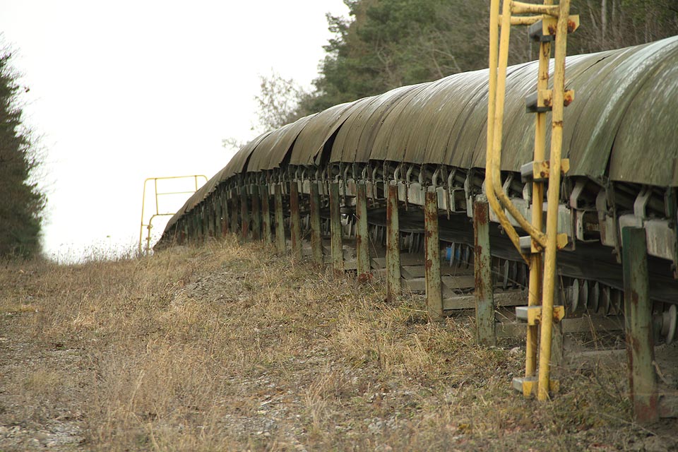 Neúnavný pracant táhne nadrcené kamení po svahu vzhůru k nebi s pravidelným skřípotem. Jeho pásy mizí kdesi v lese za obzorem.