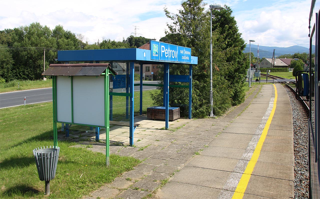 Sporá čekárna a jednoduché nástupiště v Petrově nad Desnou zastávce, vyfocené z projíždějícího vlaku Os13073 dne 2. srpna roku 2025. 