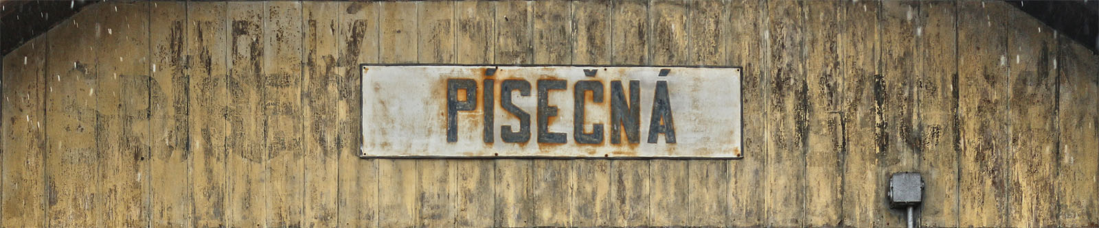 Pod plechovou cedulí na nádražním skladišti v ísečné se skrývá několik vrstev starších názvů stanice. V tomhle kraji je obvyklé, že se minulost dere nemilosrdně na povrch: Sandhübel, Sandhýbl-Supíkovice, Sandhübel-Saubsdorf, Písečná-Supíkovice a nakonec jenom Písečná - to všechno byly v historii názvy zdejší stanice.