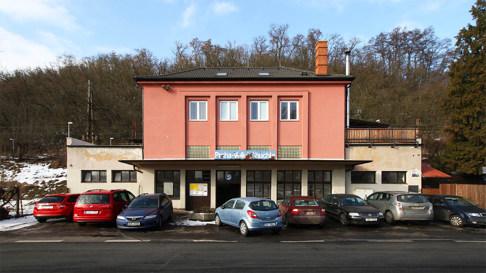 Pohled na budovu zastávky z Radotínské ulice. Praha-Velká Chuchle působí spíš jako stanice, protože disponuje čtveřicí kolejí, ostrovními nástupišti a velkolepě pojatými prostory pro cestující v budově, která však není výpravní.