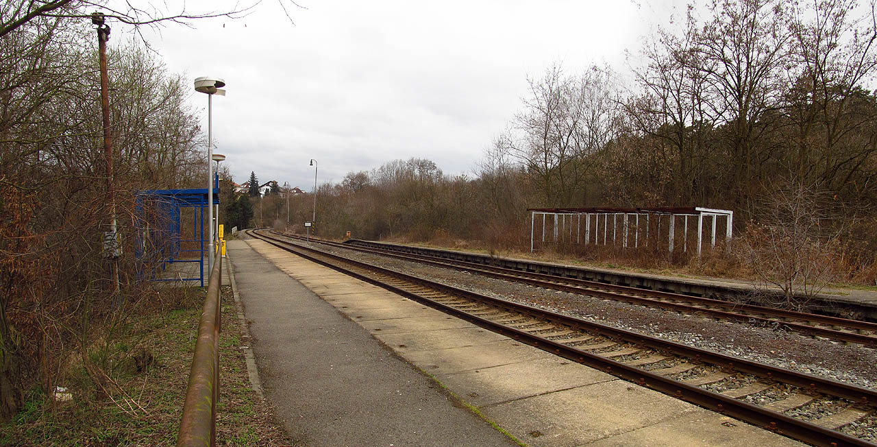 Podivná symetrie: naproti nově natřené čekárně pohlcuje džungle torzo jejího alter ega, souběžně s frekventovanou kolejí vede rezavějící a zpola rozebraný kolejový pás.