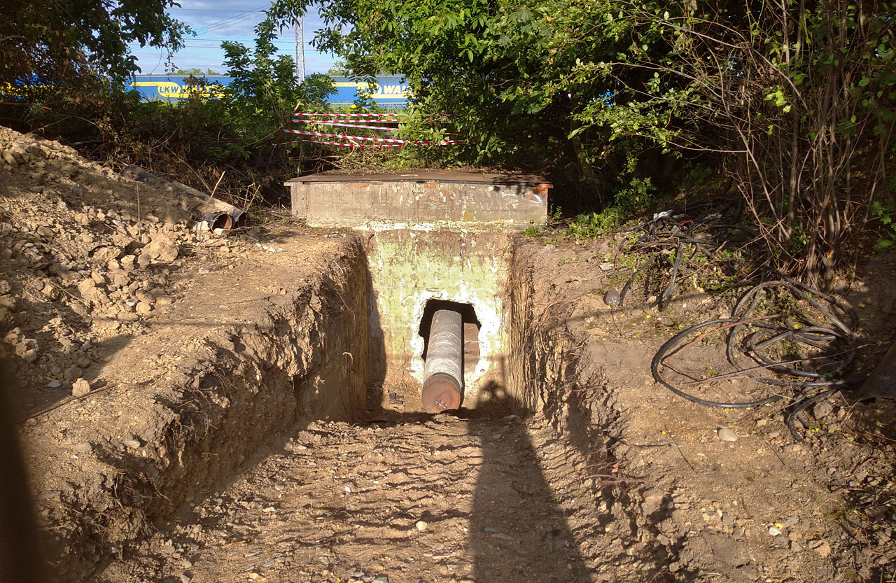Na západní straně je dobře vidět dočasná hlavice navařená na chráničce, která posloužila při jejím postupném zatahování pod železnici. Šachta tu běžně sahá nad zem jen pár desítek centimetrů. Na západní straně je dobře vidět dočasná hlavice navařená na chráničce, která posloužila při jejím postupném zatahování pod železnici. Šachta tu běžně sahá nad zem jen pár desítek centimetrů.