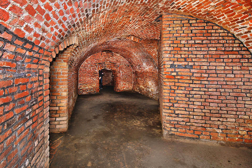 Pohled na největší z trojice podzemních sálů s valenou cihlovou klenbou. Vpravo je vidět základová zeď pseudobarokního domu, který nahradil původní hostinec v roce 1897 a protnul jeho historická sklepení.