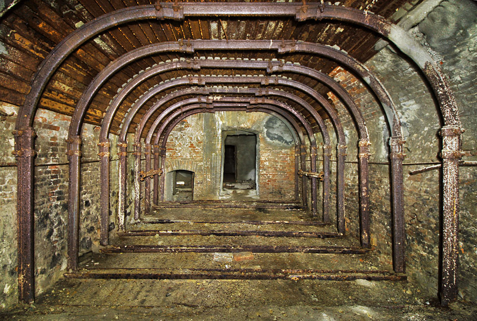 Pohled z východního sálu zpět k centrální chodbě. Vlevo je dobře vidět snížený vstup, původně schodiště, do druhého podzemního podlaží.