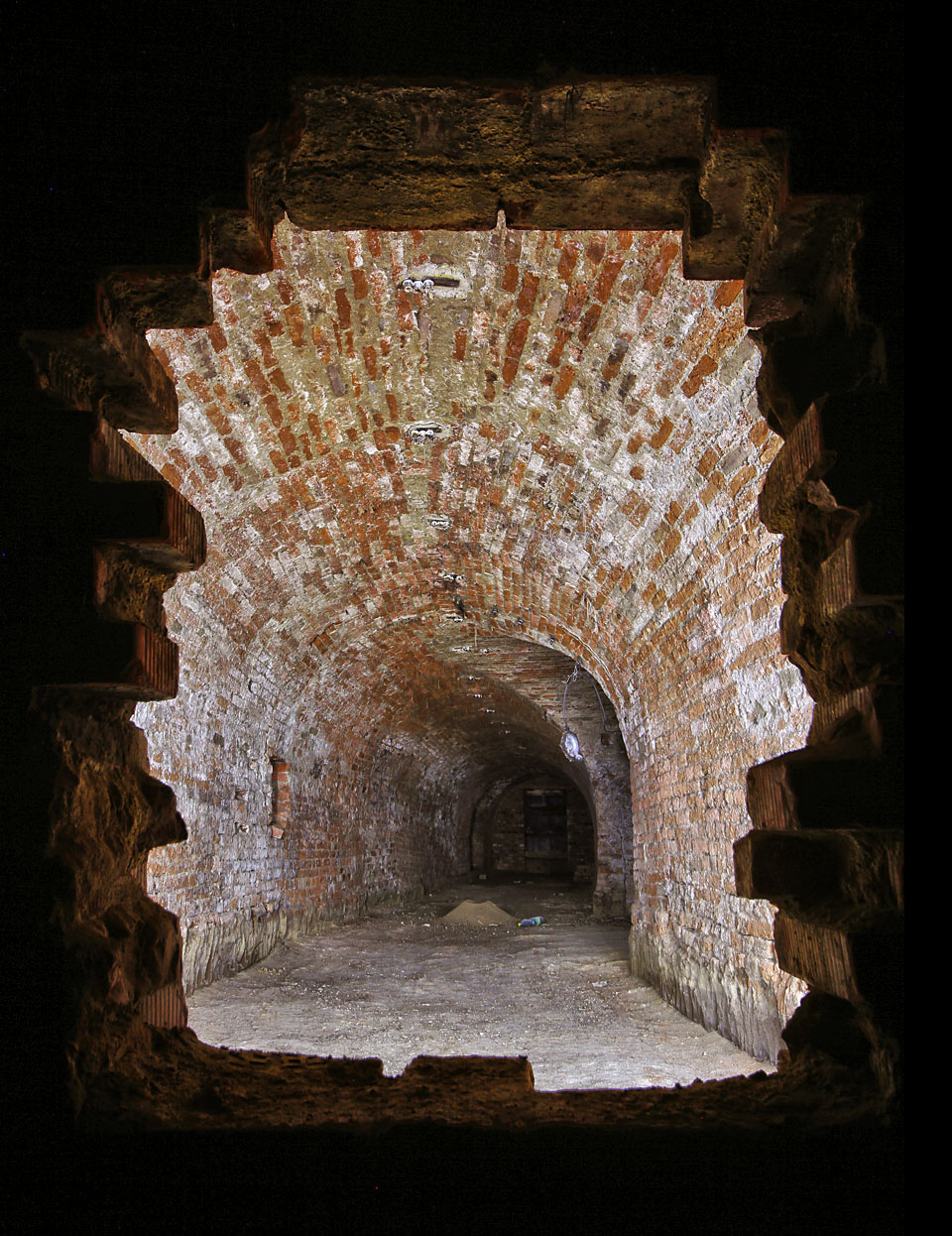 Pohled skrze příčku, která rozdělila sklepy za domem č. na přední a zadní část. Osvětlený prostor je tvořen písmenem T do směrem ulice, tmavá zadní část byla dodatečně připojena ke <a href="/Tema/Sklepy za domem Hlinky ">sklepům domu Hlinky 62</a>.